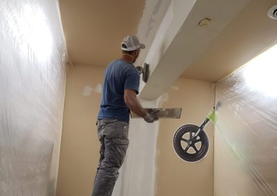 Photo of Corey applying drywall to a stuctural beam.